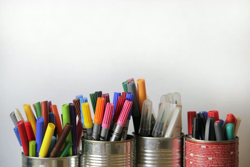 Plumones y lápices de colores organizados en botes sobre un escritorio