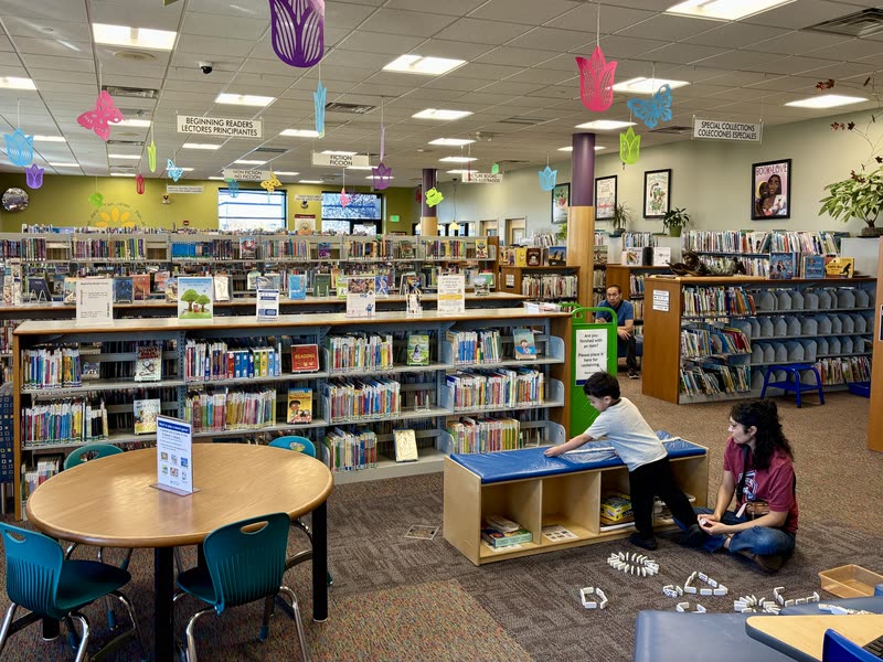 Sección infantil de una biblioteca con libros y mesas de lectura